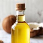 Botol minyak kelapa dara dengan kelapa segar di latar belakang.