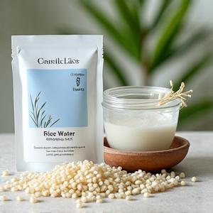 Bungkusan masker wajah dengan reka bentuk beras, di samping mangkuk berisi air beras dan biji beras mentah.